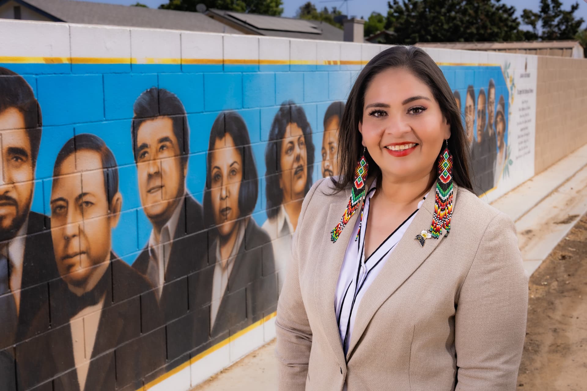 Maria Pacheco smiling in front of a community mural honoring Latino leaders